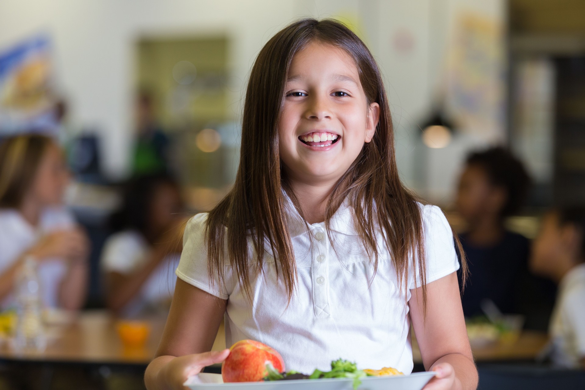 Happy elementary school student holding tray of healthy cafeteria food